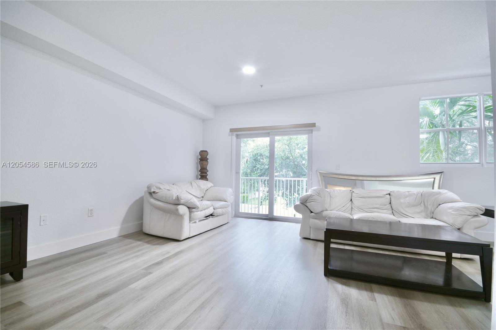 A living room features white walls, light wood-look flooring, white leather sofas, and sliding doors — 10870 NW 88th Ter # 222, Doral FL 33178, DORAL, FL