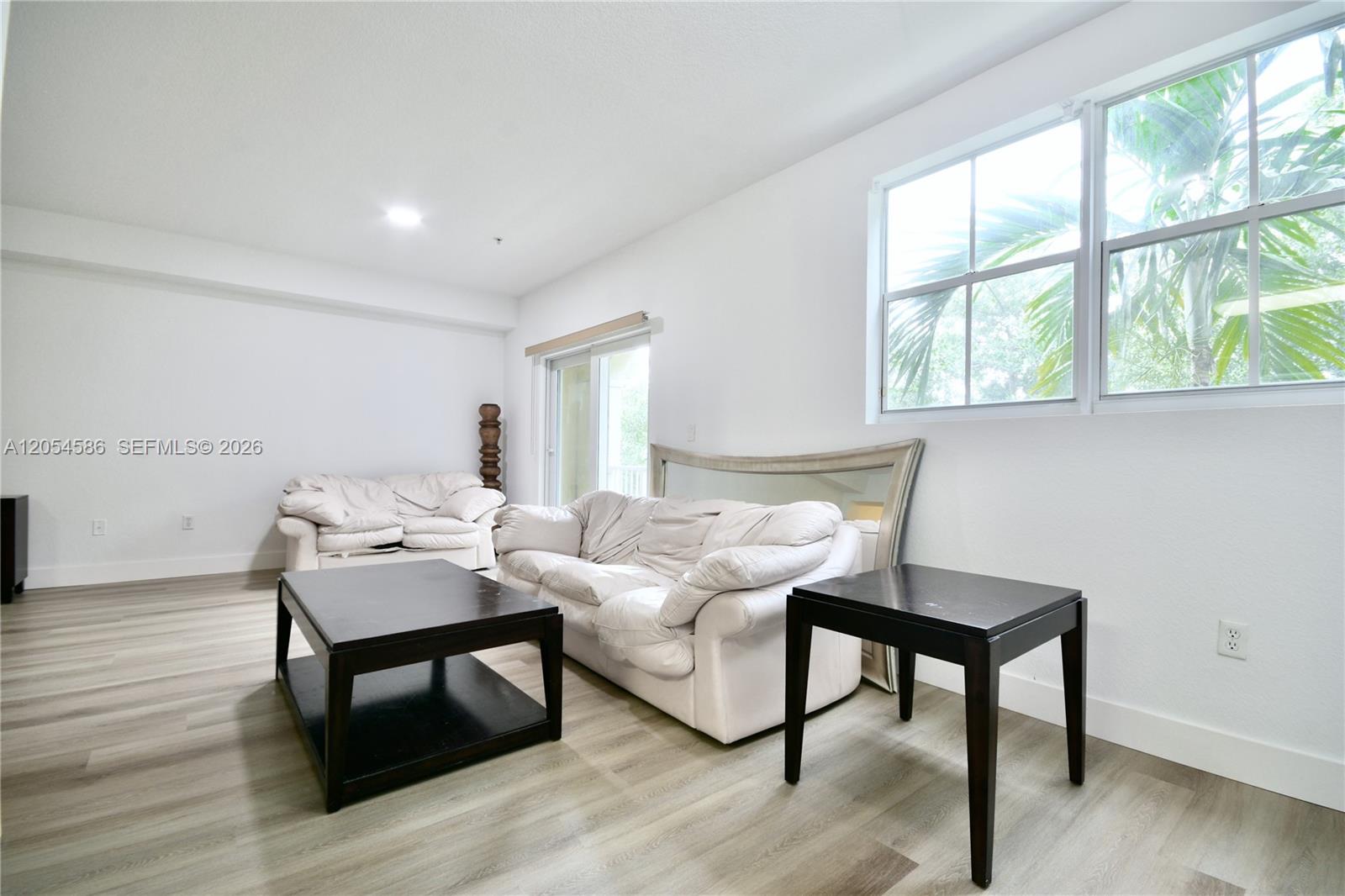 A living room features white walls, light wood-look flooring, two white sofas, and dark tables — 10870 NW 88th Ter # 222, Doral FL 33178, DORAL, FL