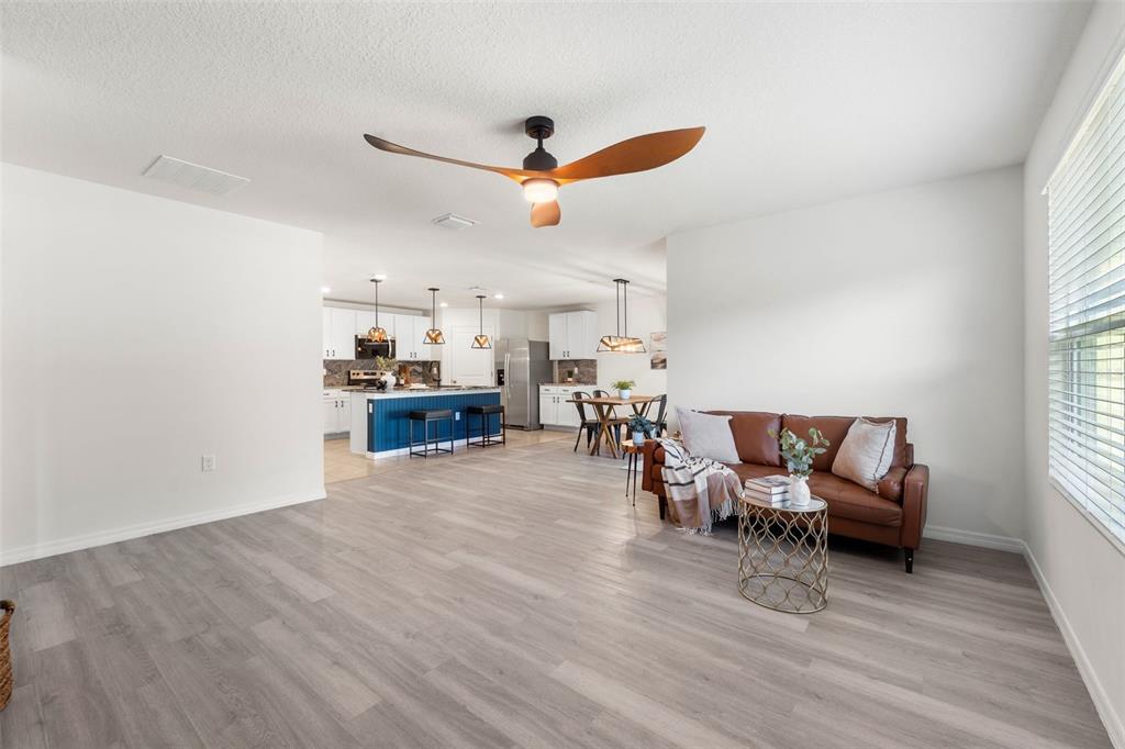 An open-concept living room features light wood-look flooring, a brown leather sofa, and a kitchen — 24596 NW 23RD LANE, NEWBERRY, FL