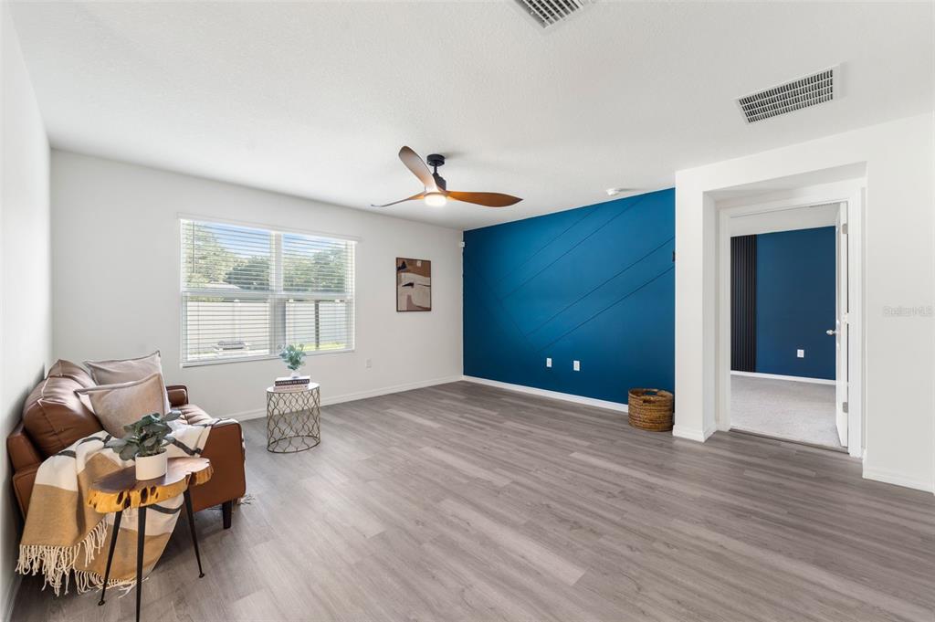 A living room features light wood-look flooring, a blue accent wall, and a leather sofa — 24596 NW 23RD LANE, NEWBERRY, FL