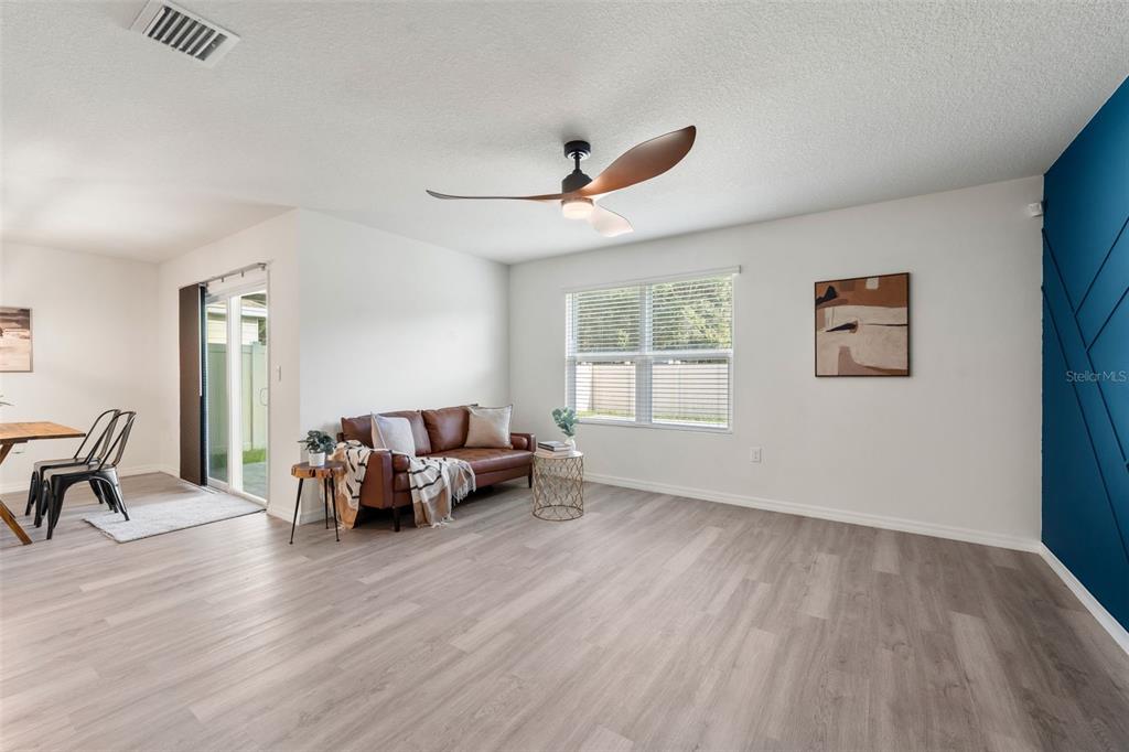 A living room features light wood-look flooring, a brown leather sofa, and a blue accent wall — 24596 NW 23RD LANE, NEWBERRY, FL