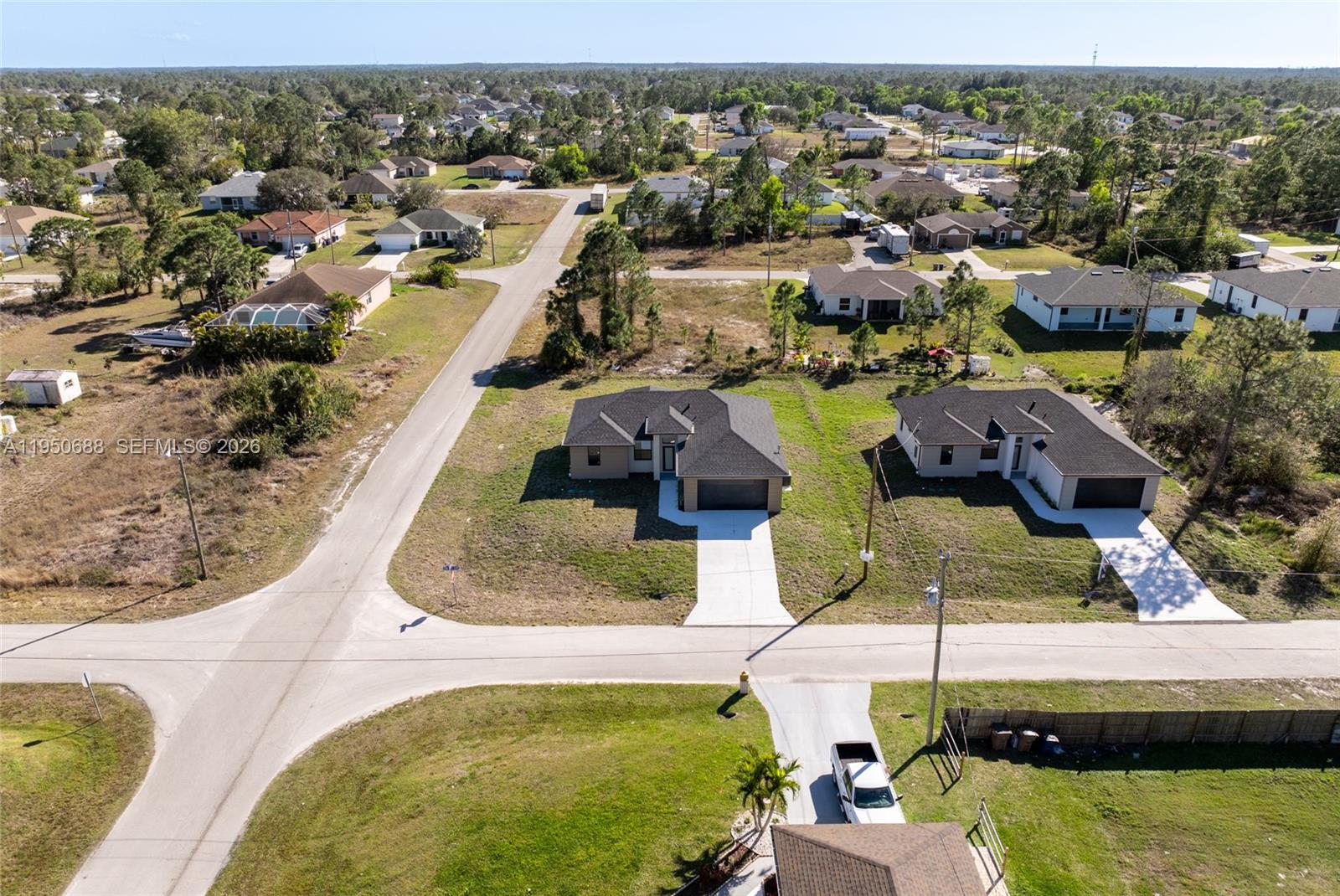 An aerial view shows two new suburban houses situated on a paved corner lot — 3601 28th St SW, Lehigh Acres FL 33976, LEHIGH ACRES, FL