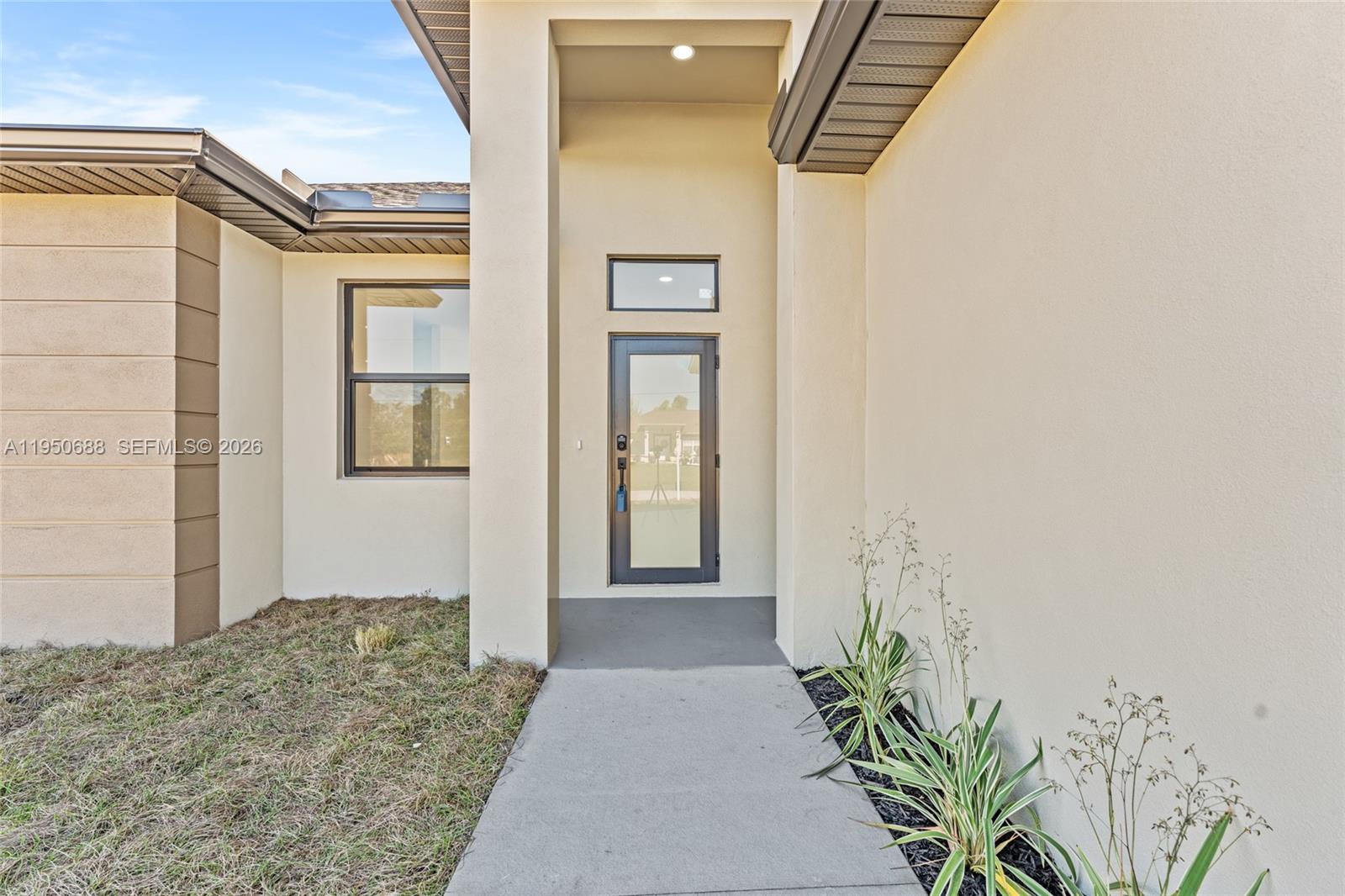 A concrete walkway leads to the front entrance of a house with beige stucco walls — 3601 28th St SW, Lehigh Acres FL 33976, LEHIGH ACRES, FL