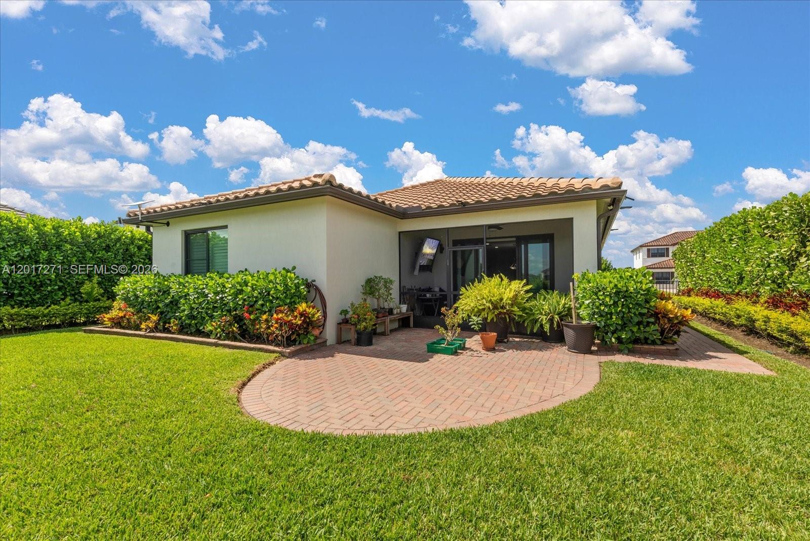 A backyard view of a house with a paved patio, screened-in porch, and lush landscaping — 4881 Iron Horse Way, Ave Maria FL 34142, AVE MARIA, FL
