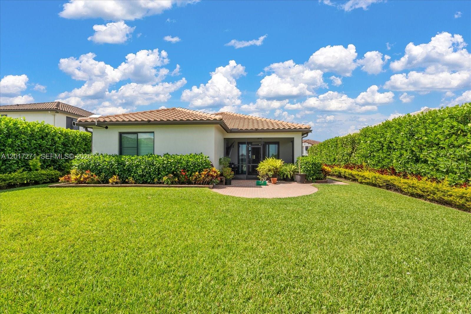 The backyard of a house features a lawn, a brick patio, and tall privacy hedges — 4881 Iron Horse Way, Ave Maria FL 34142, AVE MARIA, FL