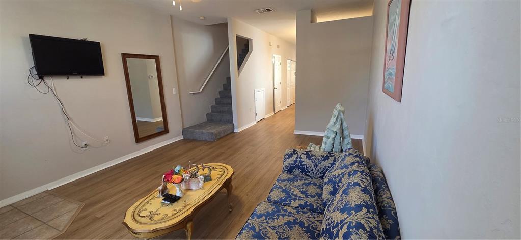 A living room features wood-look flooring, a blue patterned sofa, a coffee table, and stairs — 3970 SW 20TH AVENUE UNIT 912, GAINESVILLE, FL