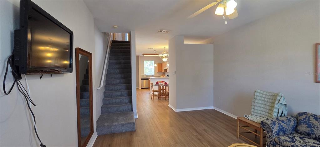 An open-concept living area features wood-look flooring, a carpeted staircase, and a view into the kitchen — 3970 SW 20TH AVENUE UNIT 912, GAINESVILLE, FL