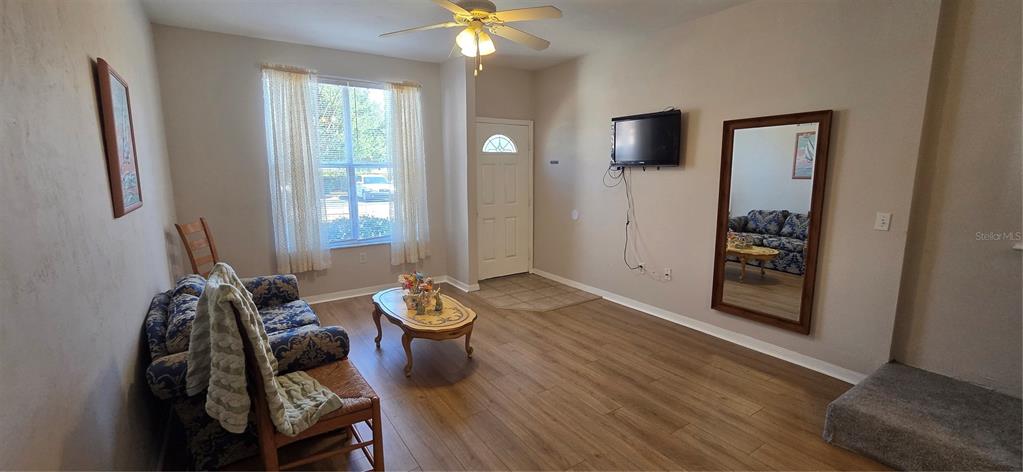 A living room features wood-look flooring, a ceiling fan, a sofa, and a wall-mounted television — 3970 SW 20TH AVENUE UNIT 912, GAINESVILLE, FL