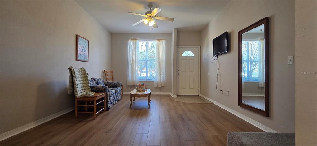 A living room features wood-look flooring, a ceiling fan, a sofa, and a wall-mounted television — 3970 SW 20TH AVENUE UNIT 912, GAINESVILLE, FL