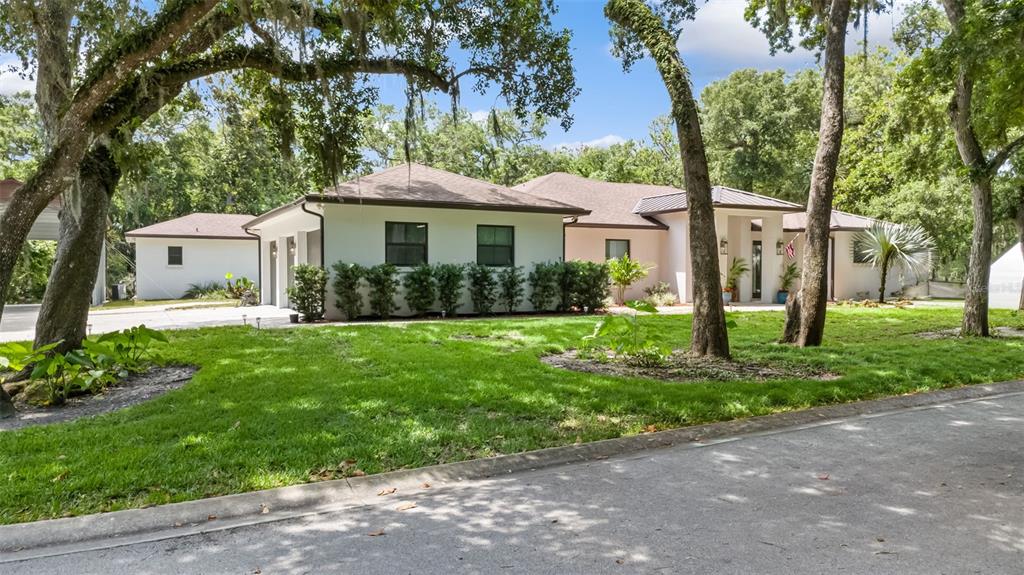 A single-story house with a white exterior, dark roof, and surrounding trees sits behind a lawn — 14 MERIDIAN HOME LANE, PALM COAST, FL