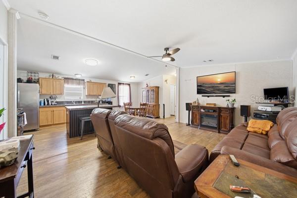 A living room features brown leather sofas, wood-look flooring, a ceiling fan, and a television — 12148 RUTHERFORD LANE, HUDSON, FL