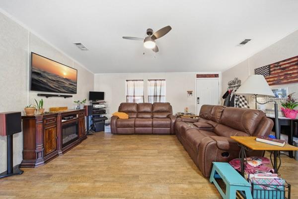 A living room with brown leather sofas, wood-look flooring, and an open kitchen area — 12148 RUTHERFORD LANE, HUDSON, FL