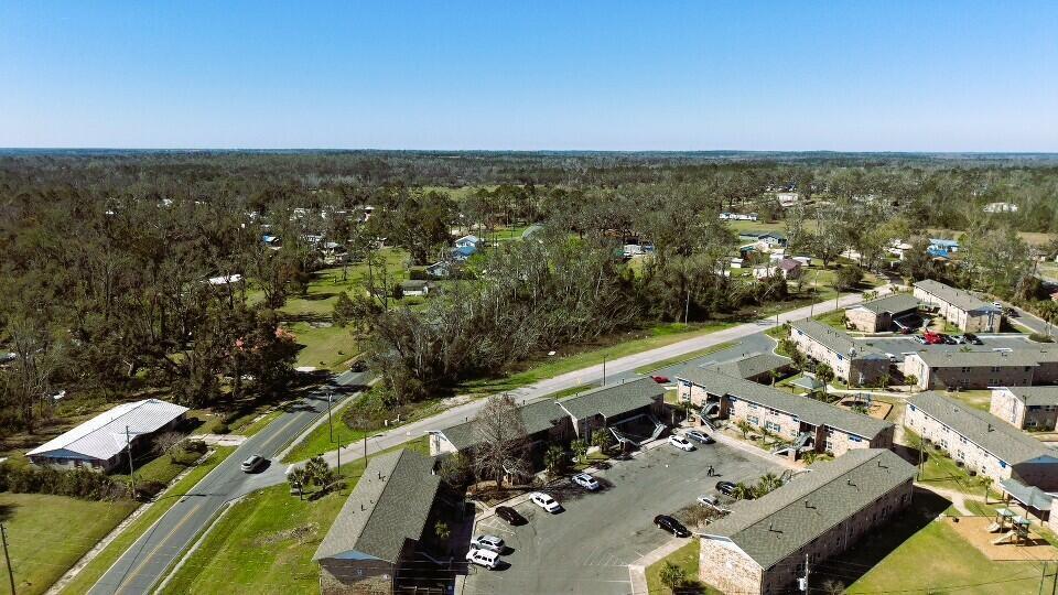 An aerial view shows apartment buildings, a parking lot, and a road surrounded by trees — Lot 7 SW Bum Gardener Drive, FL 32340, FL