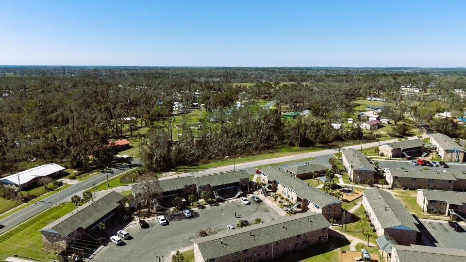 An aerial view shows a multi-building apartment complex with parking lots and surrounding wooded areas — Lot 7 SW Bum Gardener Drive, FL 32340, FL