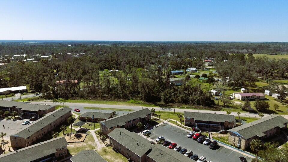 An aerial view shows a multi-building apartment complex with parking lots and surrounding wooded areas — Lot 7 SW Bum Gardener Drive, FL 32340, FL