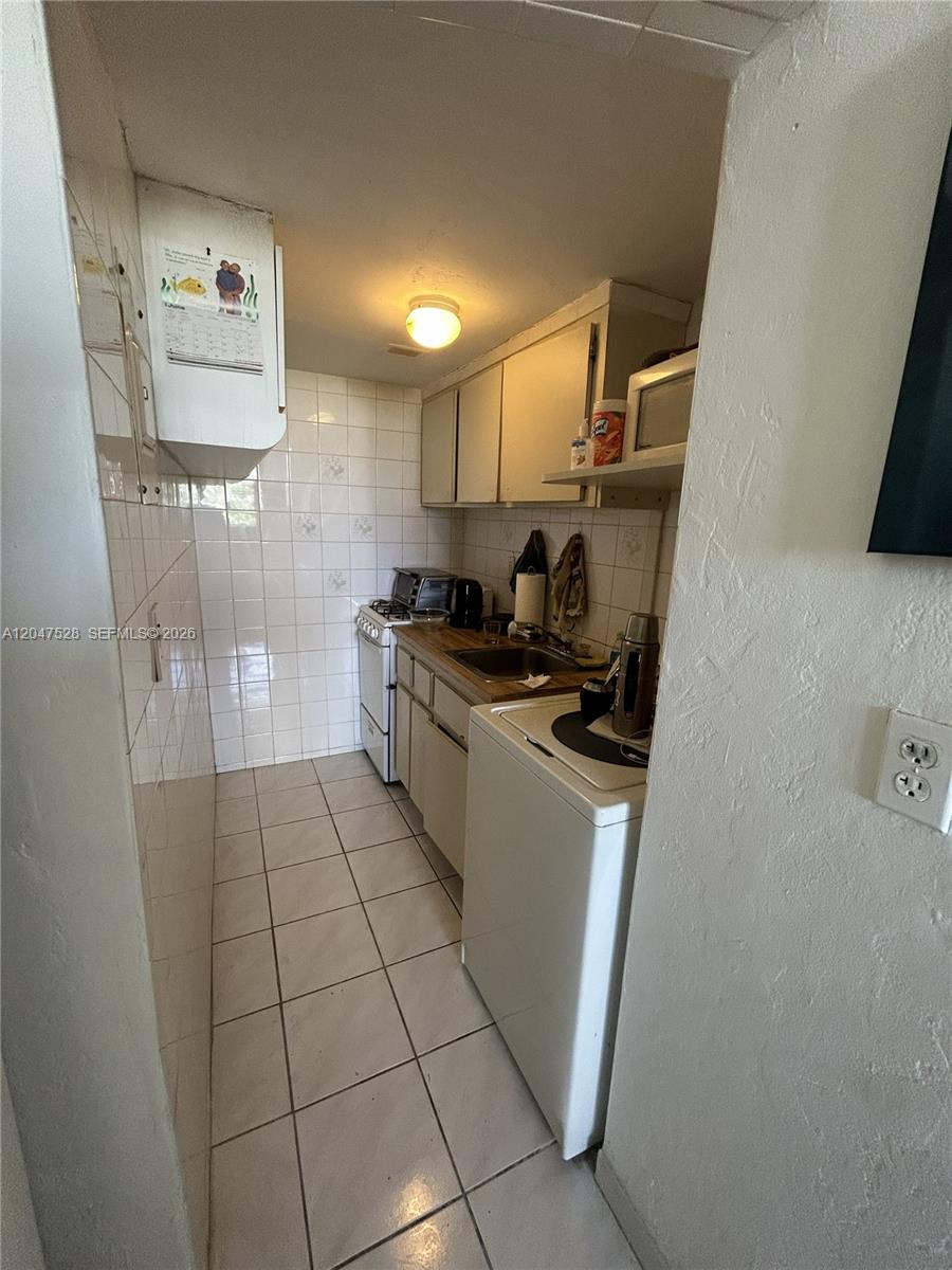 A narrow galley kitchen features white tiled walls, light-colored cabinets, and a white appliance suite — 6484 Indian Creek Dr # 303, Miami Beach FL 33141, MIAMI BEACH, FL
