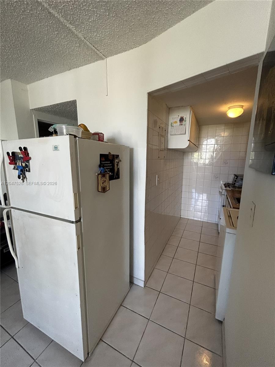 A white refrigerator stands next to a narrow, tiled kitchen with white wall tiles — 6484 Indian Creek Dr # 303, Miami Beach FL 33141, MIAMI BEACH, FL