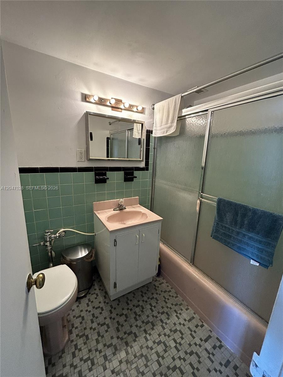 A bathroom features a pink sink and tub, green wall tiles, and a vanity cabinet — 6484 Indian Creek Dr # 303, Miami Beach FL 33141, MIAMI BEACH, FL