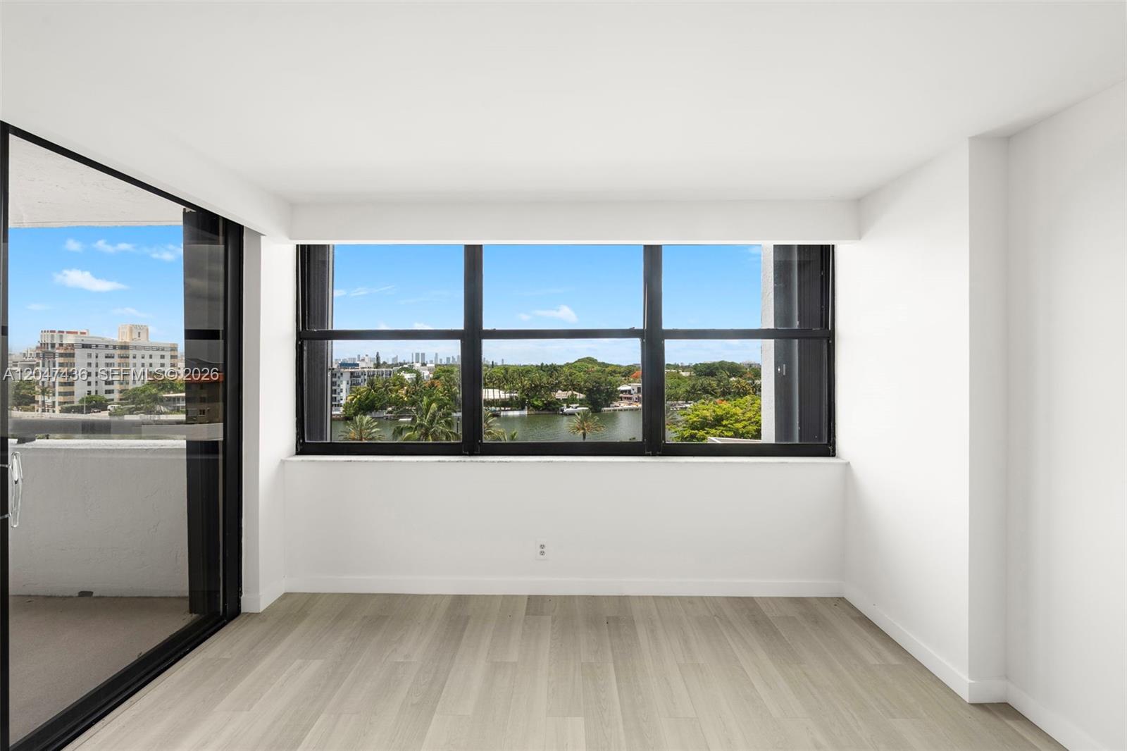 An empty room with light wood-look flooring, white walls, and a large window overlooking water — 2555 Collins Ave # 706, Miami Beach FL 33140, MIAMI BEACH, FL