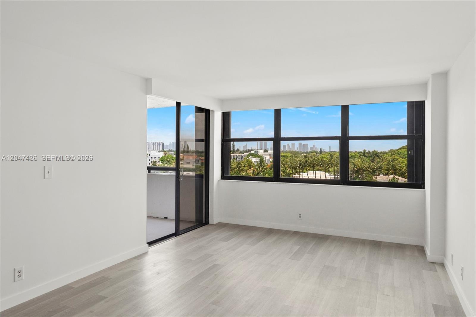 An empty room features light wood-look flooring, white walls, large windows, and a balcony door — 2555 Collins Ave # 706, Miami Beach FL 33140, MIAMI BEACH, FL