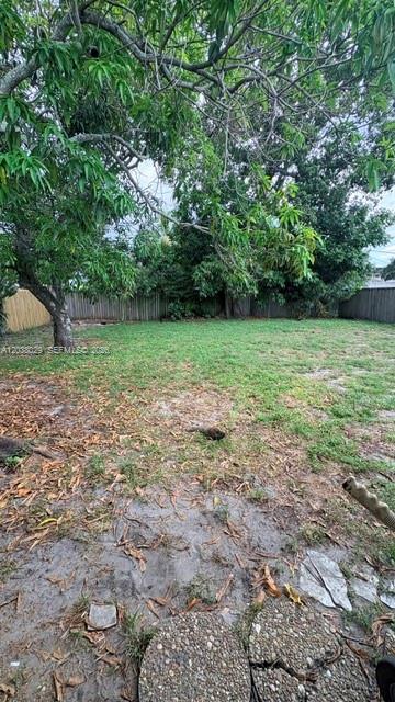 A backyard features a large tree, patchy grass, and a wooden fence in the background — 6833 SW 20th St, Miramar FL 33023, MIRAMAR, FL