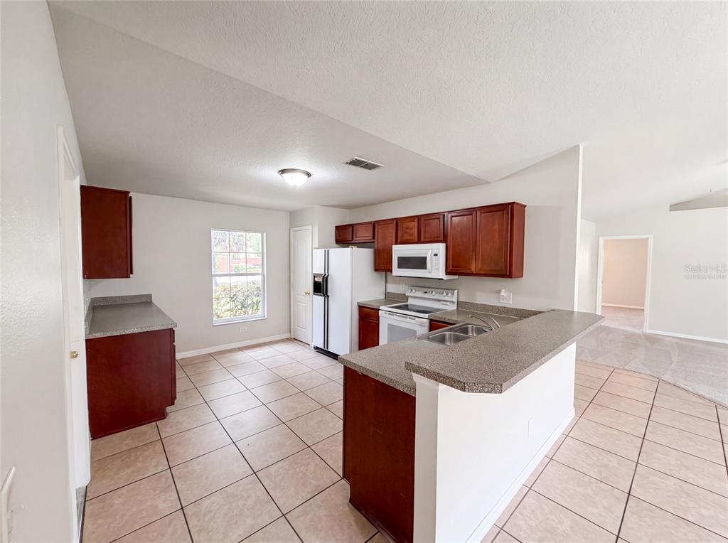 A kitchen features dark wood cabinets, laminate countertops, white appliances, and light-colored tile flooring — 306 GARDEN OAK COURT, APOPKA, FL