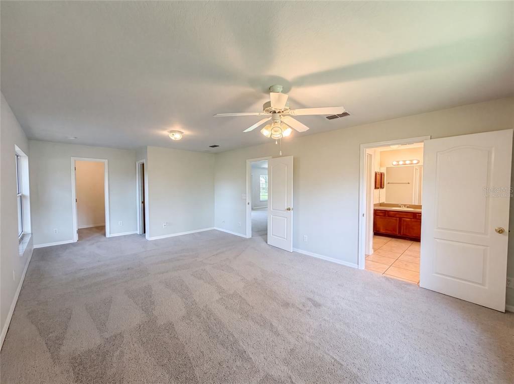 A carpeted bedroom features a ceiling fan, multiple doorways, and an attached bathroom with tile — 306 GARDEN OAK COURT, APOPKA, FL