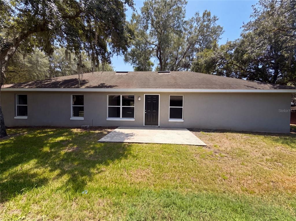 The rear exterior of a single-story house features a concrete patio and a black door — 306 GARDEN OAK COURT, APOPKA, FL