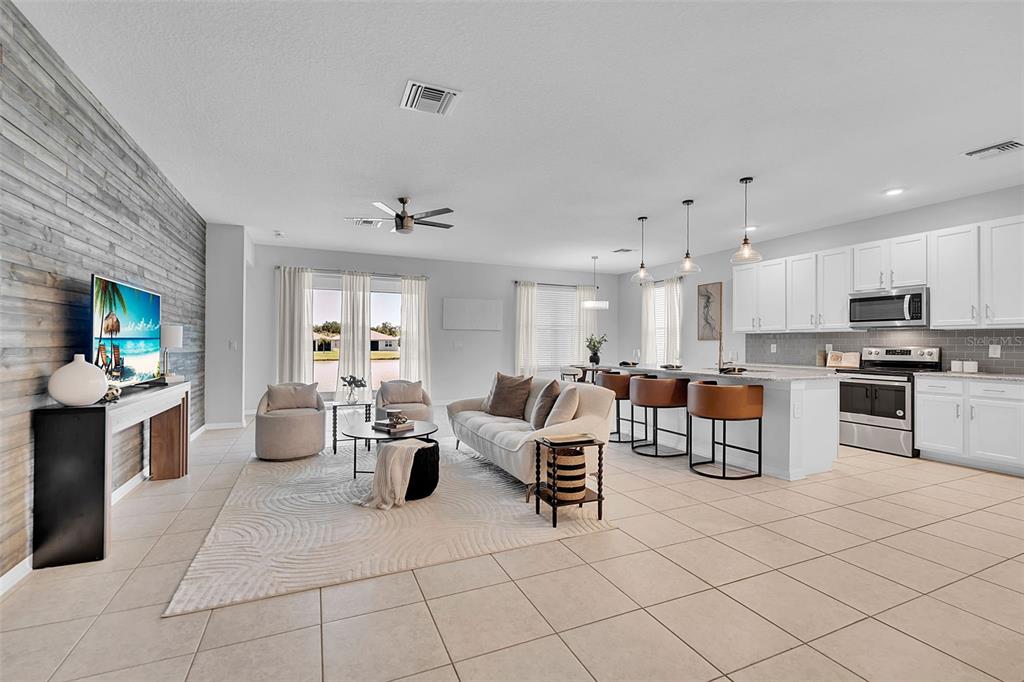 An open-concept living room and kitchen with white cabinetry, tile floors, and a wood-paneled wall — 4505 WINDY HAMMOCK WAY, PALMETTO, FL