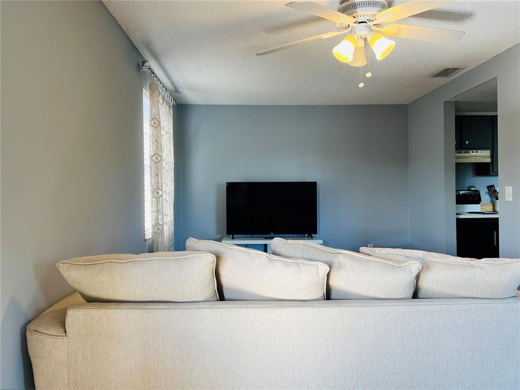 A living room features a light-colored sofa facing a television on a white stand — 5026 WATER OAK DRIVE UNIT 208, BRADENTON, FL