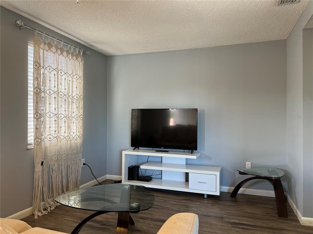 A living room features gray walls, wood-look flooring, a white media console, and macramé curtains — 5026 WATER OAK DRIVE UNIT 208, BRADENTON, FL