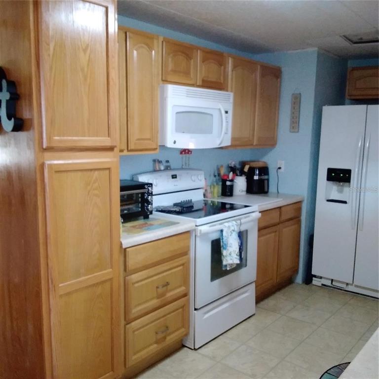 A kitchen features light wood cabinets, white appliances, and light blue walls — 10473 HOLIDAY SHORES DRIVE UNIT 303, LARGO, FL