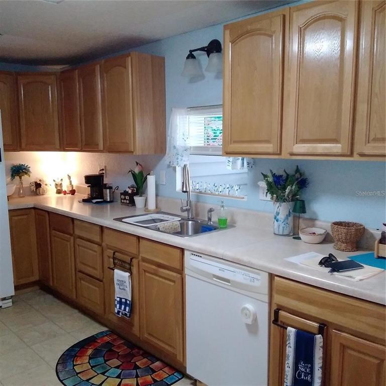 A kitchen with light wood cabinets, white countertops, a double sink, and a white dishwasher — 10473 HOLIDAY SHORES DRIVE UNIT 303, LARGO, FL