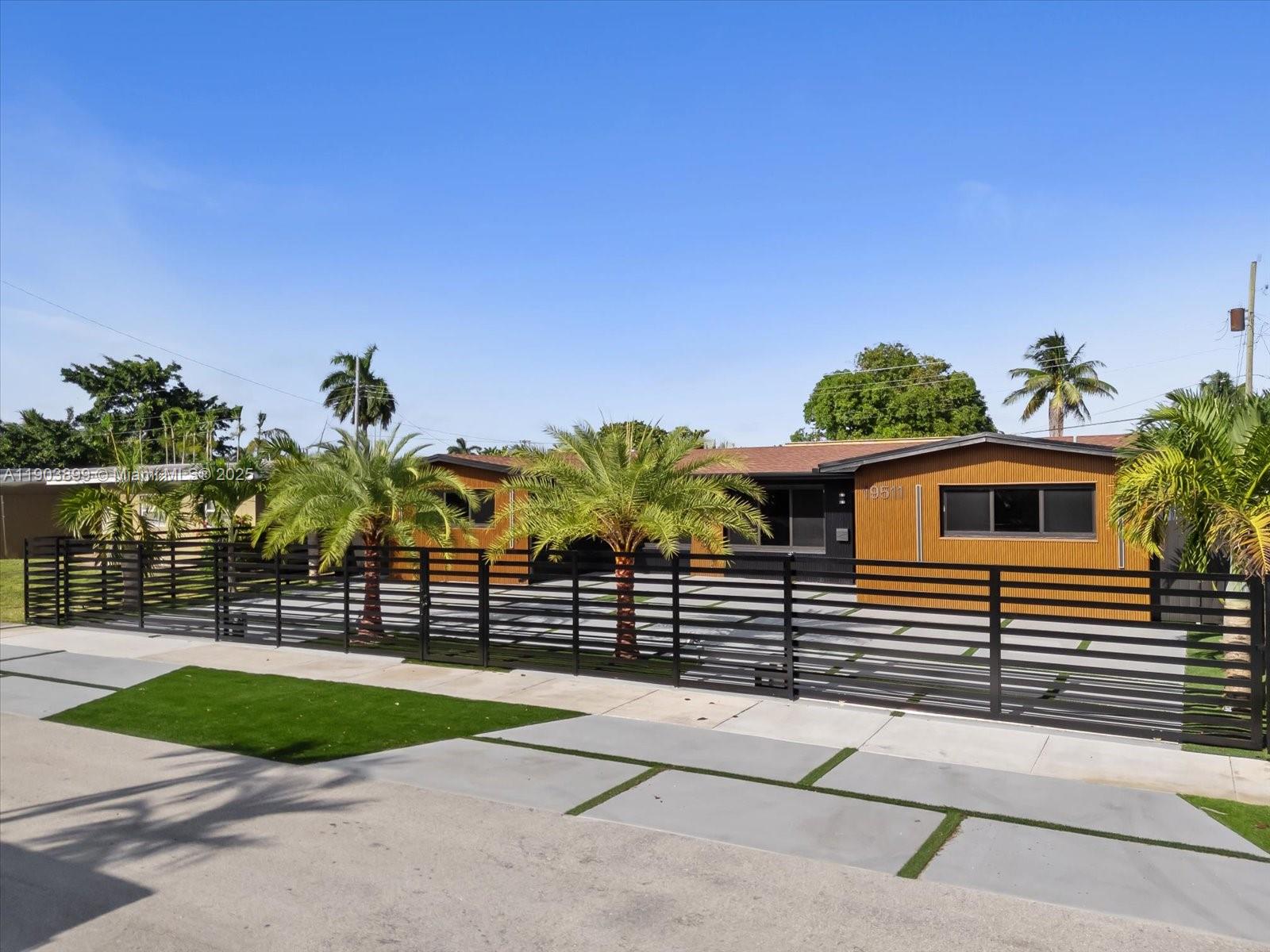 A single-story house with wood-paneled siding sits behind a modern black horizontal slat fence — 19511 NE 18th Pl # 0, Miami FL 33179, MIAMI, FL