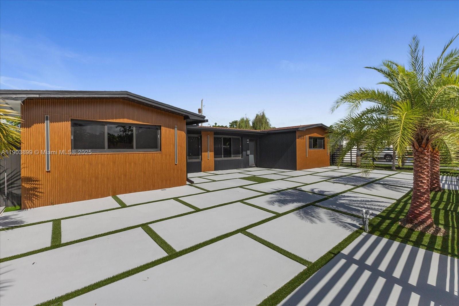 A modern house exterior features wood-slat siding, black accents, and a large paver driveway — 19511 NE 18th Pl # 0, Miami FL 33179, MIAMI, FL