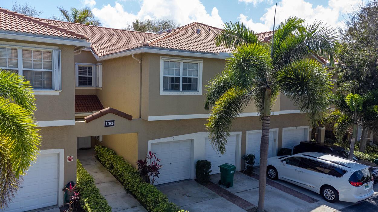 An exterior view of a two-story tan townhouse with a tiled roof and attached garages — 110 Lighthouse Circle # H, Tequesta FL 33469, TEQUESTA, FL