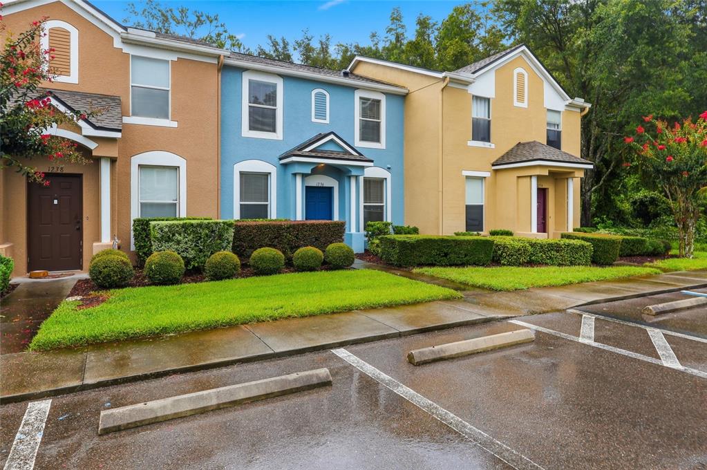 A row of three colorful townhouses with manicured hedges and a paved parking lot in front — 1236 BLENHEIM COURT, WESLEY CHAPEL, FL