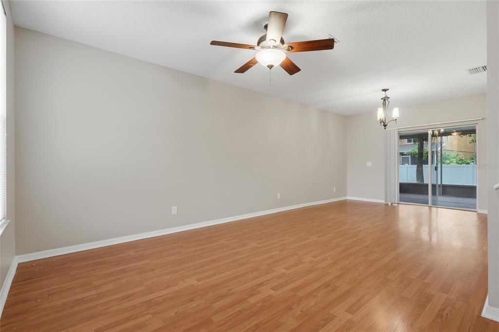 An empty living room features light-colored walls, wood-look flooring, a ceiling fan, and sliding glass doors — 1236 BLENHEIM COURT, WESLEY CHAPEL, FL