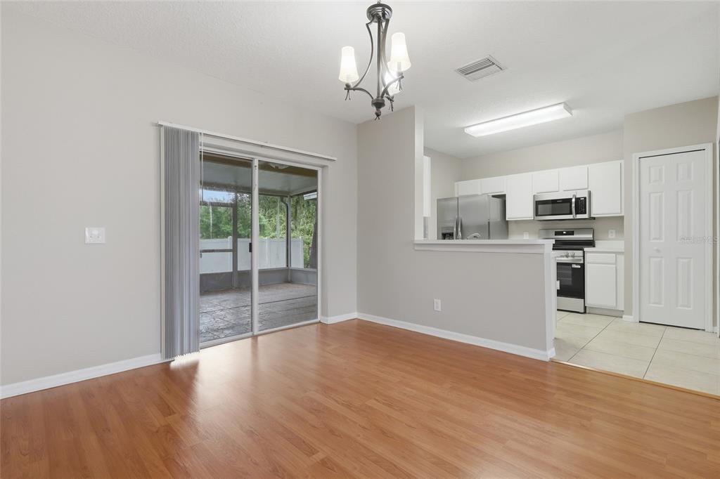 A dining area with wood flooring, a sliding glass door, and an adjacent open kitchen — 1236 BLENHEIM COURT, WESLEY CHAPEL, FL