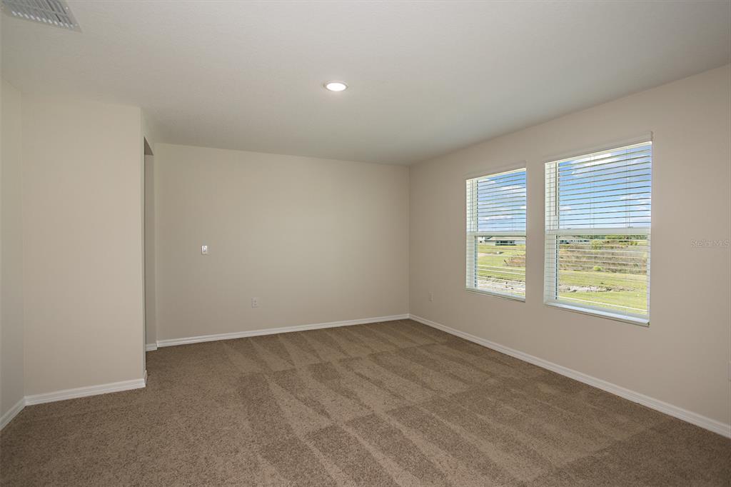 An empty bedroom with beige walls, tan carpet, and two windows overlooking a grassy field — 4438 RIVERBEND BOULEVARD, HAINES CITY, FL