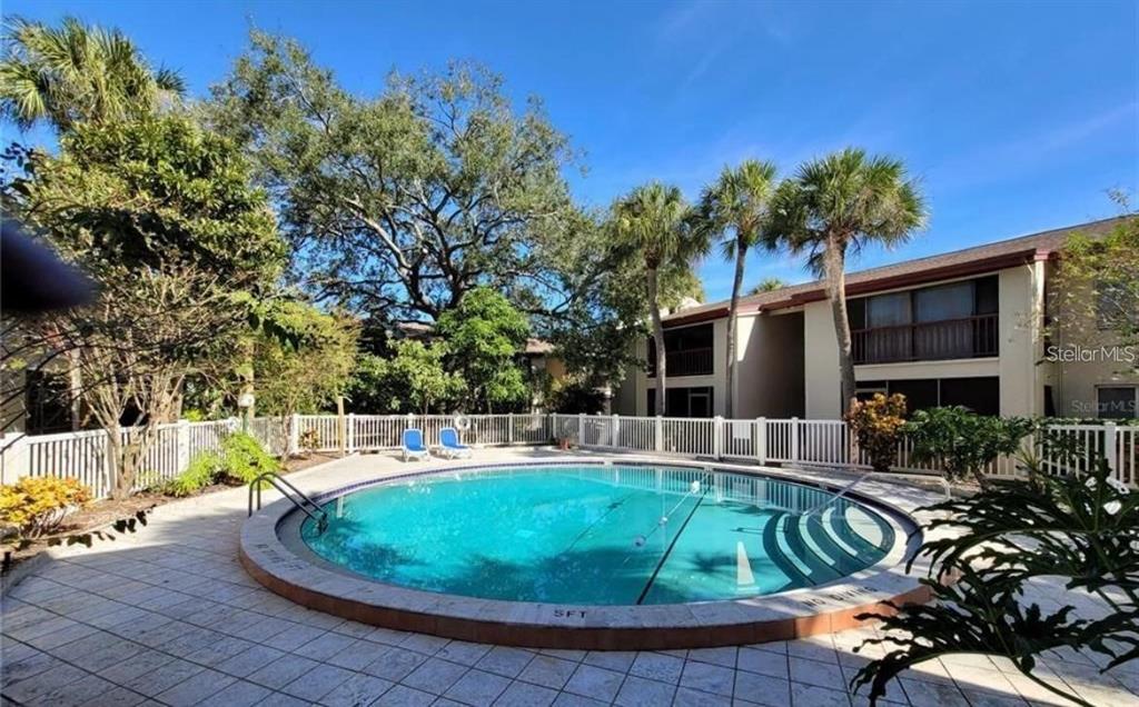 A circular swimming pool is surrounded by a tiled deck, white fencing, and palm trees — 3850 N LAKE DRIVE UNIT 140, TAMPA, FL