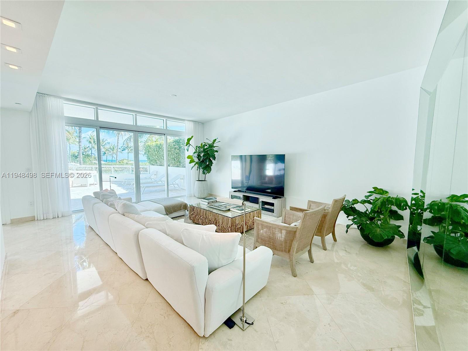 A bright living room features white furniture, marble floors, and sliding glass doors to a patio — 50 S Pointe Dr, Miami Beach FL 33139, MIAMI BEACH, FL