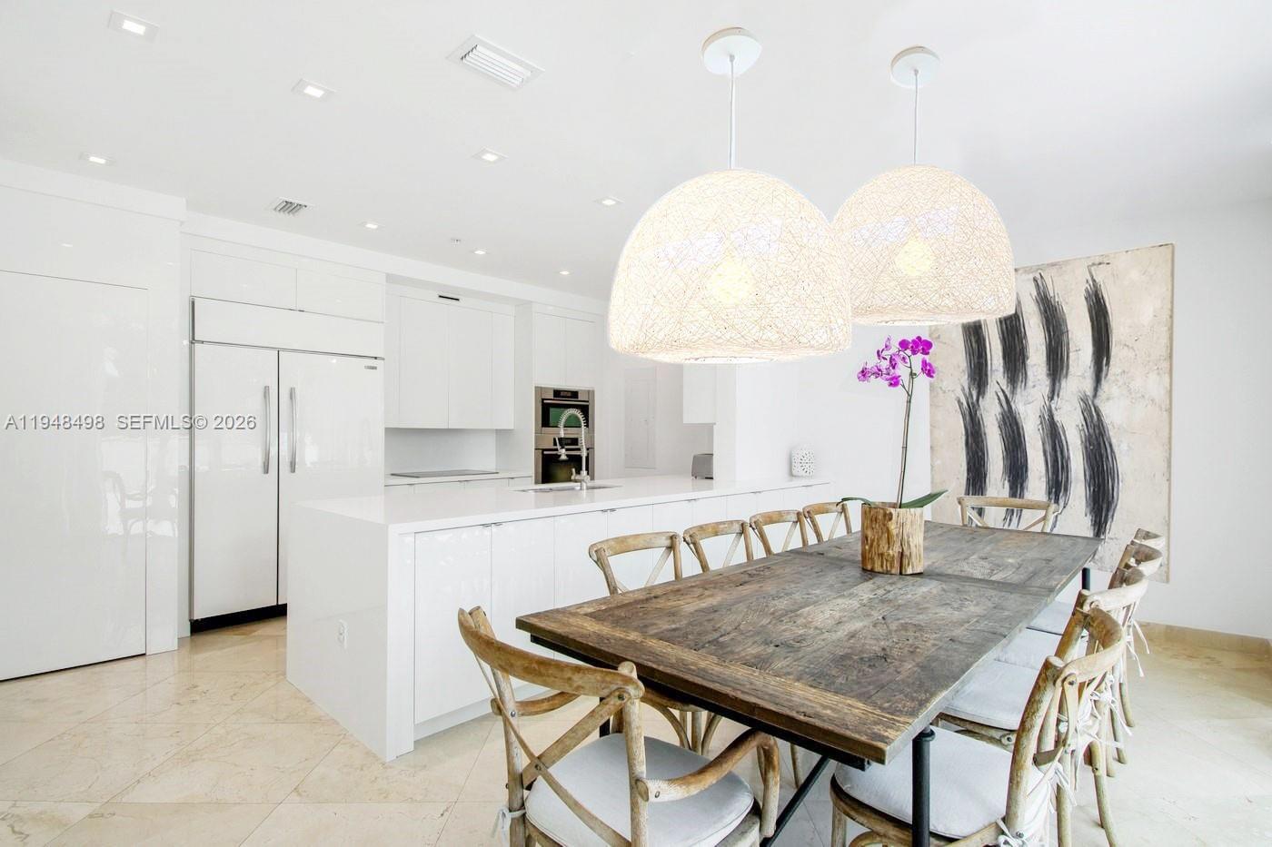 A modern white kitchen features a large island and a rustic wooden dining table — 50 S Pointe Dr, Miami Beach FL 33139, MIAMI BEACH, FL