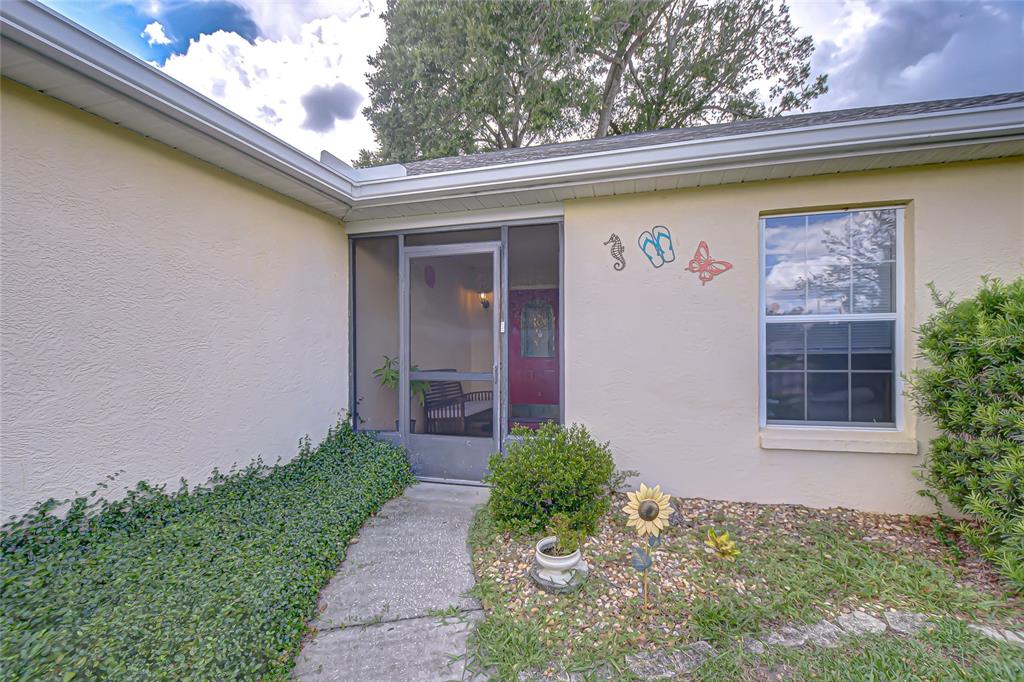 The exterior of a house features a screened entryway, a window, and decorative wall art — 6911 OAKCREST WAY, ZEPHYRHILLS, FL