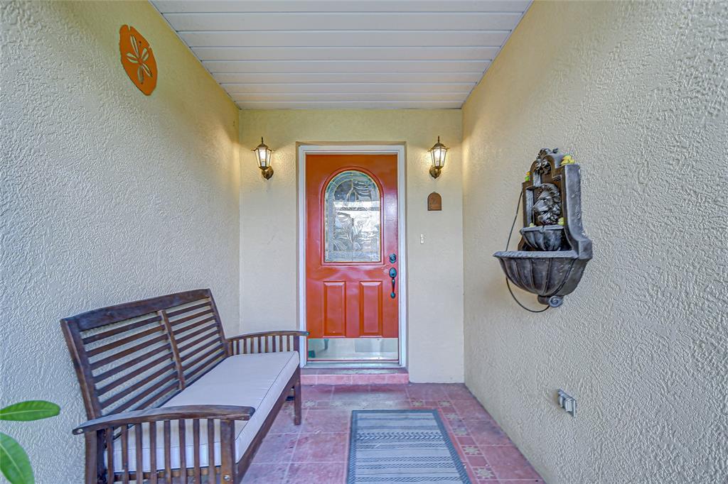 A covered entryway features a wooden bench, a wall-mounted fountain, and a red front door — 6911 OAKCREST WAY, ZEPHYRHILLS, FL