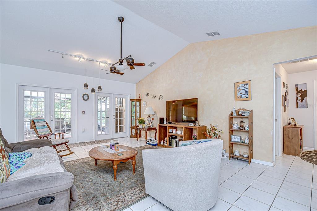 A living room features a vaulted ceiling, tile flooring, a ceiling fan, and glass doors — 6911 OAKCREST WAY, ZEPHYRHILLS, FL
