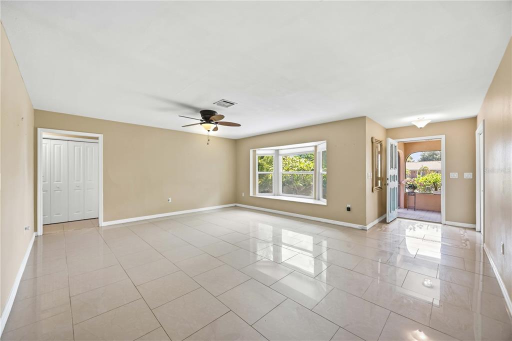 An empty living room features beige walls, large light-colored floor tiles, a ceiling fan, and a bay window — 2317 GOYA DRIVE, NOKOMIS, FL