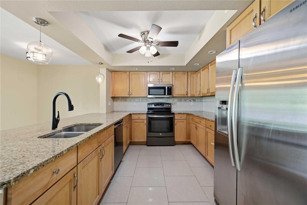 A kitchen features light wood cabinets, granite countertops, stainless steel appliances, and tile flooring — 2317 GOYA DRIVE, NOKOMIS, FL