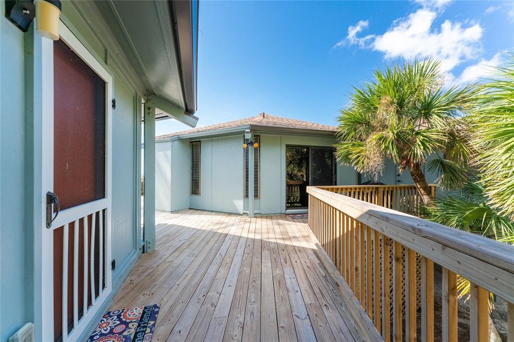 A wooden deck connects two light blue exterior structures under a bright blue sky — 6580 MANASOTA KEY ROAD, ENGLEWOOD, FL