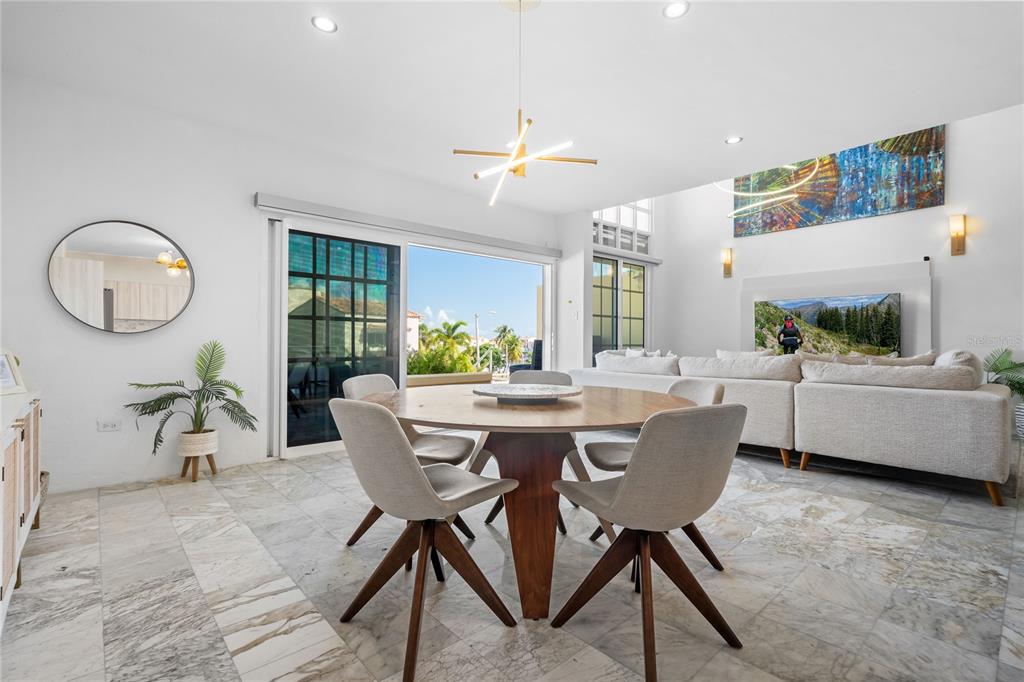 A dining area with a round wooden table and chairs sits before a sliding glass door — 115 HARBOUR DRIVE UNIT 8, HUMACAO, PR